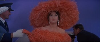 Movie still from “What a Way to Go!” (1964), directed by J. Lee Thompson – A woman wearing a large orange hat and a dress; Medium shot, Low angle