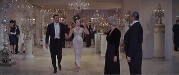 Movie still from “What a Way to Go!” (1964), directed by J. Lee Thompson – A group of people standing in a room with chandeliers in the background; Wide shot, Over the shoulder angle