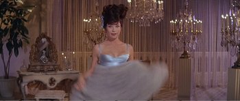 Movie still from “What a Way to Go!” (1964), directed by J. Lee Thompson – A beautiful woman in a blue dress in front of a chandelier; Medium shot, Low angle