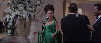 Movie still from “What a Way to Go!” (1964), directed by J. Lee Thompson – A woman in a green dress standing next to a man in a suit; Medium shot, Over the shoulder angle