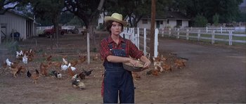 Movie still from “What a Way to Go!” (1964), directed by J. Lee Thompson – A woman holding a bowl of food while standing next to chickens in a field; Medium shot, Low angle
