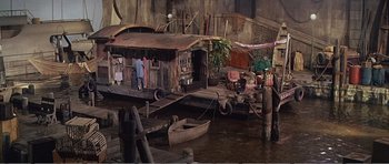 Movie still from “What a Way to Go!” (1964), directed by J. Lee Thompson – A boat sits in the water next to a dock; Wide shot, High angle