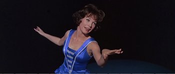 Movie still from “What a Way to Go!” (1964), directed by J. Lee Thompson – A woman in a blue dress is holding her arms out; Medium shot, Low angle