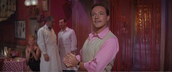 Movie still from “What a Way to Go!” (1964), directed by J. Lee Thompson – A man in a pink shirt claps his hands; Medium shot, Low angle
