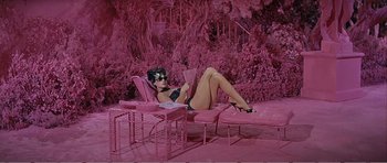 Movie still from “What a Way to Go!” (1964), directed by J. Lee Thompson – A woman laying on a pink chair reading a book; Wide shot, High angle