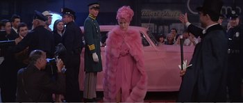 Movie still from “What a Way to Go!” (1964), directed by J. Lee Thompson – A woman in a pink fur coat standing in front of a car; Wide shot, Low angle
