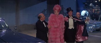 Movie still from “What a Way to Go!” (1964), directed by J. Lee Thompson – A man and a woman in a pink fur coat and a man in a tuxedo; Medium shot, Low angle