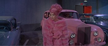 Movie still from “What a Way to Go!” (1964), directed by J. Lee Thompson – A woman in a pink fur coat holding a pink purse; Wide shot, High angle