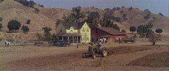 Movie still from “What a Way to Go!” (1964), directed by J. Lee Thompson – A man on a tractor in a dirt field near houses; Extreme Wide shot, High angle