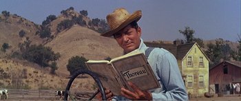 Movie still from “What a Way to Go!” (1964), directed by J. Lee Thompson – A man wearing a straw hat is reading a book; Medium shot, Low angle