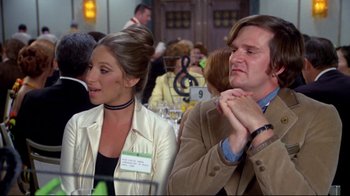 Movie still from “What's Up, Doc?” (1972), directed by Peter Bogdanovich – A man and a woman sitting next to each other at an event; Medium shot, Over the shoulder angle
