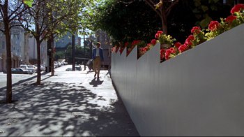 Movie still from “What's Up, Doc?” (1972), directed by Peter Bogdanovich – A woman walking down a sidewalk next to a white fence; Wide shot, Low angle