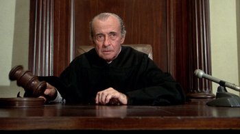 Movie still from “What's Up, Doc?” (1972), directed by Peter Bogdanovich – An older man sitting at a table in a courtroom; Close Up shot, Low angle