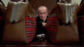 Movie still from “What's Up, Doc?” (1972), directed by Peter Bogdanovich – An old man is peeking out of two suitcases; Medium shot, High angle