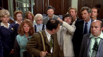 Movie still from “What's Up, Doc?” (1972), directed by Peter Bogdanovich – A group of people standing around a man in a brown suit; Medium shot, Over the shoulder angle