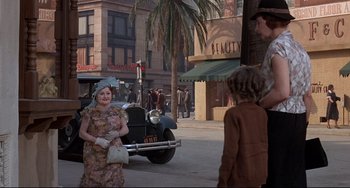 Movie still from “What's the Matter with Helen?” (1971), directed by Curtis Harrington – An older woman standing in front of an old car on the street; Wide shot, Over the shoulder angle