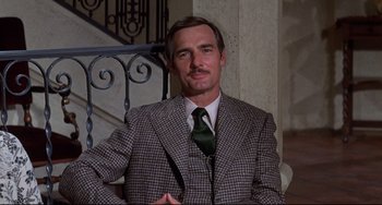 Movie still from “What's the Matter with Helen?” (1971), directed by Curtis Harrington – A man wearing a suit and tie sitting in a chair; Medium shot, Low angle