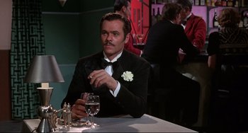 Movie still from “What's the Matter with Helen?” (1971), directed by Curtis Harrington – A man sitting at a table with a glass of wine; Medium shot, Over the shoulder angle
