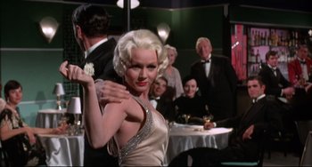 Movie still from “What's the Matter with Helen?” (1971), directed by Curtis Harrington – A blonde woman in a white dress dancing in front of a group of people; Medium shot, Low angle
