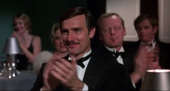 Movie still from “What's the Matter with Helen?” (1971), directed by Curtis Harrington – A man in a tuxedo clapping in front of other people; Close Up shot, Over the shoulder angle