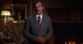 Movie still from “What's the Matter with Helen?” (1971), directed by Curtis Harrington – A man in a suit and tie standing in front of a painting; Medium shot, Low angle