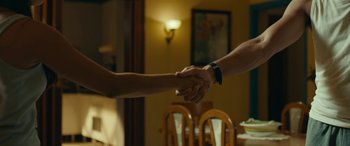 Movie still from “Sevillanas de Brooklyn” (2021), directed by Vicente Villanueva – Two people are shaking hands in front of a table; Medium shot, Over the shoulder angle