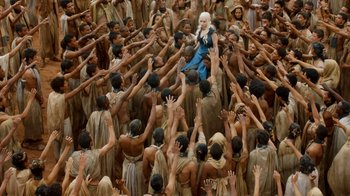 Movie still from “Game of Thrones” (2011), created by D.B. Weiss – Daenerys targaryen riding a horse surrounded by a crowd of men; Wide shot, Overhead angle