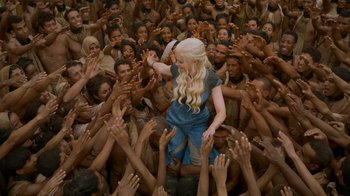Movie still from “Game of Thrones” (2011), created by D.B. Weiss – A group of people reaching up to touch a statue of daenerys targaryen from game of thrones; Wide shot, High angle