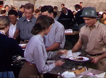 Movie still from “When Worlds Collide” (1951), directed by Rudolph Maté – A group of people standing around plates of food on a table; Medium shot, High angle