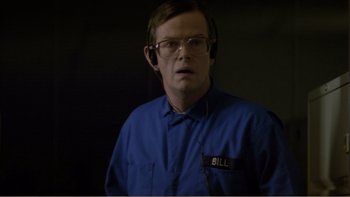 Movie still from “When a Man Falls” (2007), directed by Ryan Eslinger – A man wearing a blue shirt and glasses; Medium shot, Low angle