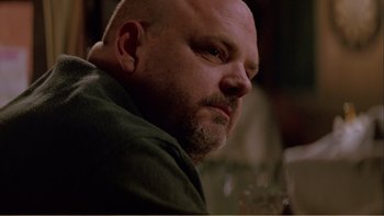 Movie still from “When a Man Falls” (2007), directed by Ryan Eslinger – A man with a shaved head and a goatee is sitting at a table with a glass of wine in front of him; Close Up shot, Low angle