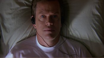 Movie still from “When a Man Falls” (2007), directed by Ryan Eslinger – A man laying in a bed wearing headphones; Close Up shot, Overhead angle