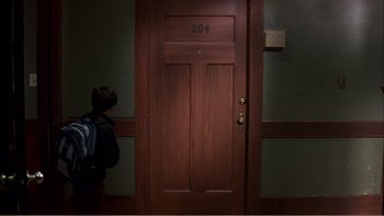 Movie still from “When a Man Falls” (2007), directed by Ryan Eslinger – A person standing in front of a wooden door; Wide shot, High angle
