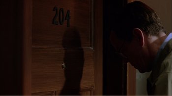 Movie still from “When a Man Falls” (2007), directed by Ryan Eslinger – A shadow of a person standing in front of a wooden door; Close Up shot, High angle
