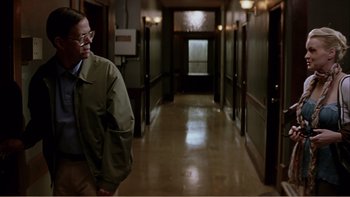 Movie still from “When a Man Falls” (2007), directed by Ryan Eslinger – A man wearing glasses walking down a hall way; Medium shot, Over the shoulder angle