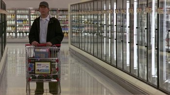 Movie still from “When a Man Falls” (2007), directed by Ryan Eslinger – A man pushing a shopping cart in a grocery store; Wide shot, High angle