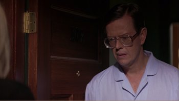 Movie still from “When a Man Falls” (2007), directed by Ryan Eslinger – A man with glasses is standing in front of a wooden door; Close Up shot, Low angle