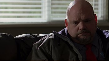Movie still from “When a Man Falls” (2007), directed by Ryan Eslinger – A bald man sitting on a couch looking sad; Close Up shot, Low angle