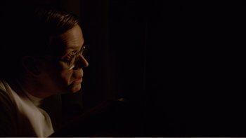 Movie still from “When a Man Falls” (2007), directed by Ryan Eslinger – A man with glasses is looking out a window at night; Close Up shot, Low angle
