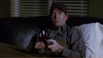 Movie still from “When a Man Falls” (2007), directed by Ryan Eslinger – A man sitting on a couch holding a glass of wine; Medium shot, High angle