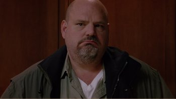 Movie still from “When a Man Falls” (2007), directed by Ryan Eslinger – A bald man with a beard and a jacket on; Close Up shot, Low angle