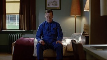 Movie still from “When a Man Falls” (2007), directed by Ryan Eslinger – A man sitting on a bed in a room; Medium shot, Low angle