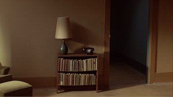 Movie still from “When a Man Falls” (2007), directed by Ryan Eslinger – A lamp and a book shelf in a room; Wide shot, High angle