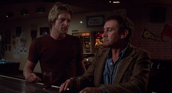 Movie still from “When a Stranger Calls” (1979), directed by Fred Walton – Two men sitting at a table in front of a bar; Medium shot, Low angle