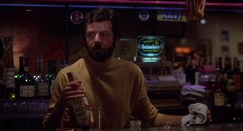 Movie still from “When a Stranger Calls” (1979), directed by Fred Walton – A man sitting at a bar holding a bottle of alcohol; Close Up shot, Over the shoulder angle