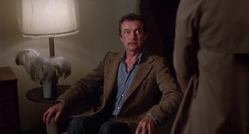 Movie still from “When a Stranger Calls” (1979), directed by Fred Walton – A man sitting in a chair wearing a jacket; Medium shot, Over the shoulder angle