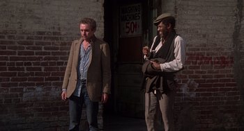 Movie still from “When a Stranger Calls” (1979), directed by Fred Walton – A man standing next to another man in a hat; Medium shot, Low angle