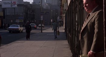 Movie still from “When a Stranger Calls” (1979), directed by Fred Walton – A person walking down a sidewalk near a building; Wide shot, Over the shoulder angle