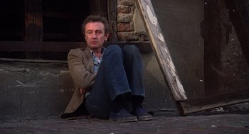 Movie still from “When a Stranger Calls” (1979), directed by Fred Walton – A man sitting on the ground in front of a building; Medium shot, High angle