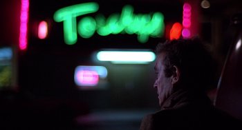 Movie still from “When a Stranger Calls” (1979), directed by Fred Walton – A man standing in front of a neon sign at night; Close Up shot, Low angle